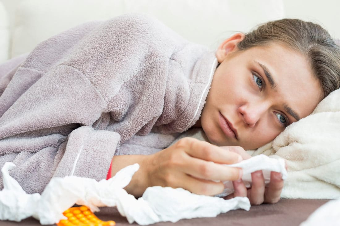 Sick woman with tissue and medicines lying on bed