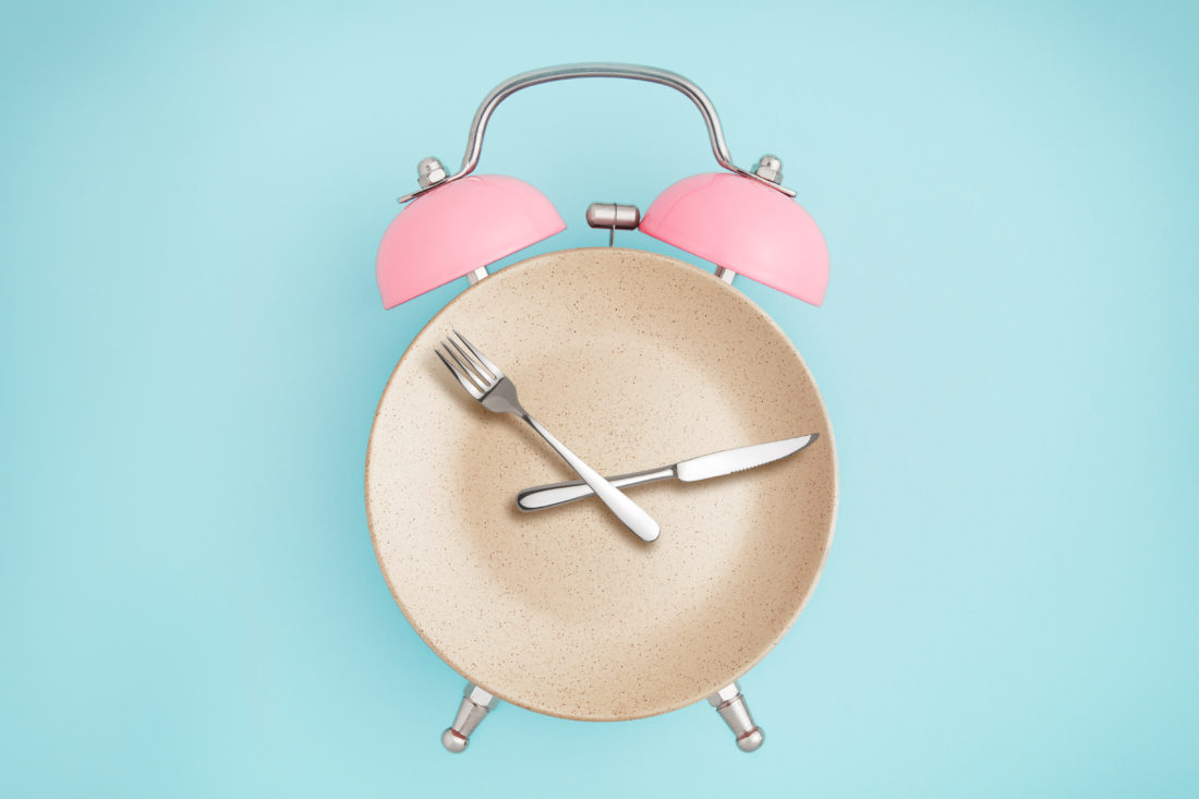 Alarm clock and plate with cutlery . Concept of intermittent fasting, lunchtime, diet and weight loss