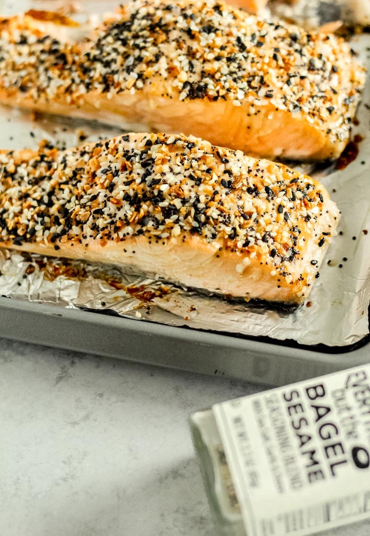 Everything bagel salmon on a foil-lined baking sheet with everything bagel seasoning next to it. 