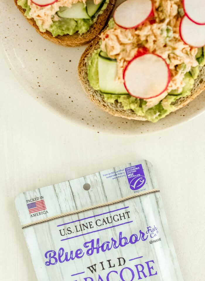 Spicy tuna salad on avocado toast next to a pouch of sustainable wild albacore tuna.