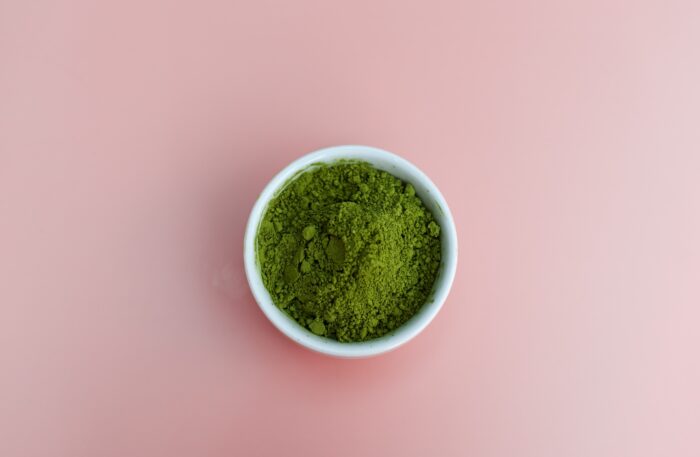 a white ceramic dish filled with green powder; the background is pale pink