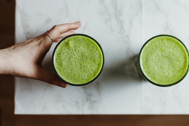  A woman reaching for a glass of Athletic Greens that is sitting on a marble counter