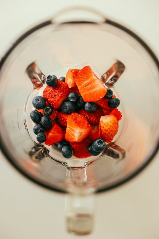 Overhead view of inside blender with strawberries and blueberries inside it. 