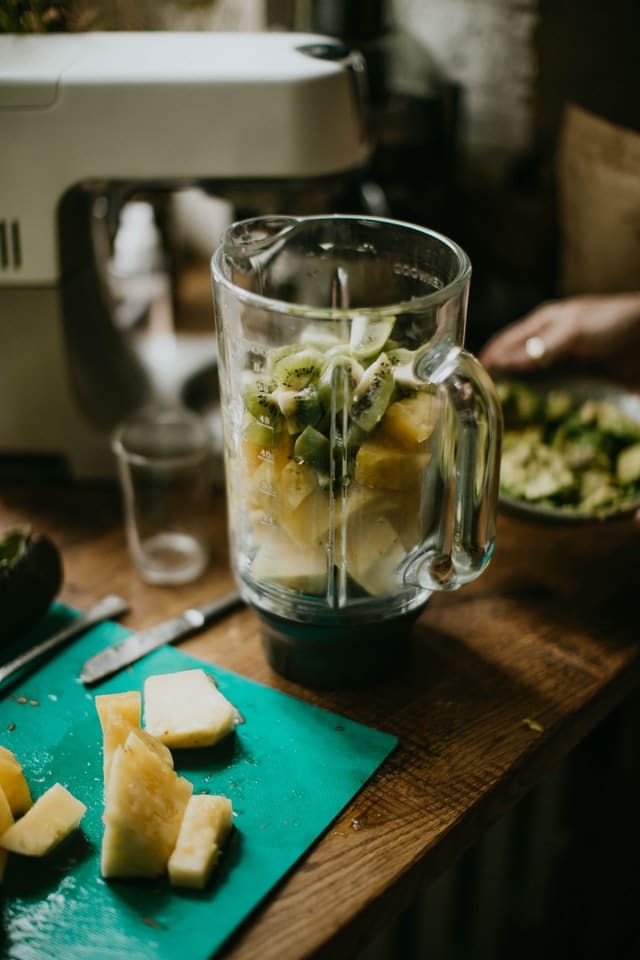 Does blending destroy nutrients? Picture of blender on wooden table with fruit inside and cut pineapple next to it. 