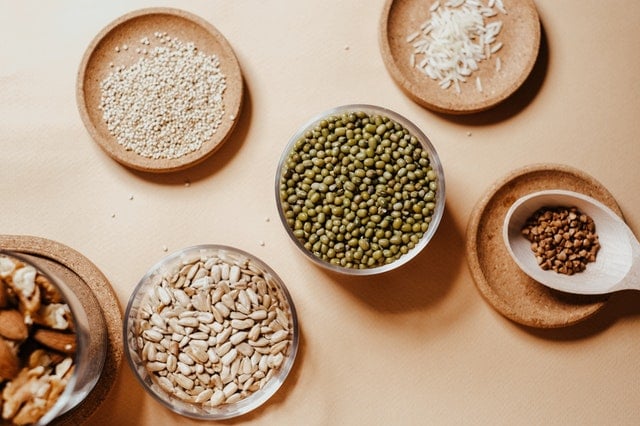 Overhead view of grains, seeds, nuts, and peas in small wooden and glass bowls. 