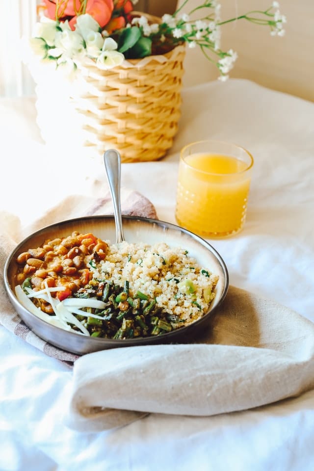 Bowl of quinoa, beans, and veggies with a glass of orange juice. next to a basket of flowers.